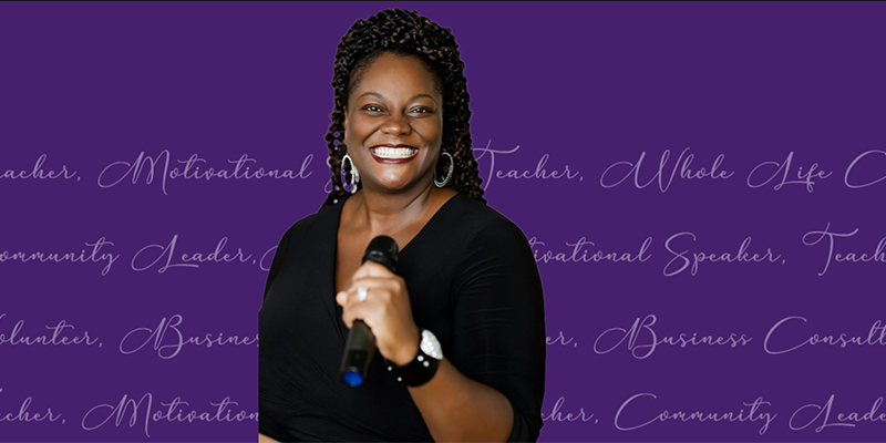 Smiling Black woman in a black top holding a microphone, speaking at a motivational event with a purple backdrop of cursive phrases.